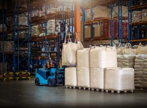 Forklift is handling jumbo bags in large warehouse.